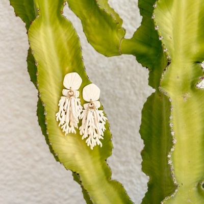 Brincos creme pendurados em folhas verdes de planta