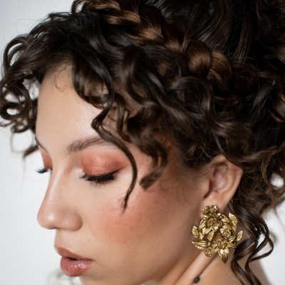 Mulher com cabelo cacheado e brinco dourado floral