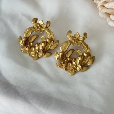 Brincos dourados de flores sobre tecido branco com flores cor-de-rosa