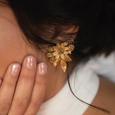 Brinco dourado em forma de flores em orelha com mão tocando rosto
