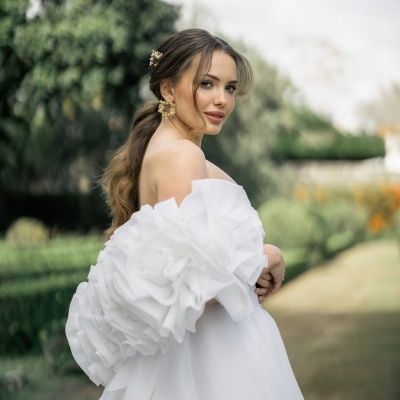 Noiva com vestido branco de mangas volumosas e acessórios dourados no cabelo e orelhas