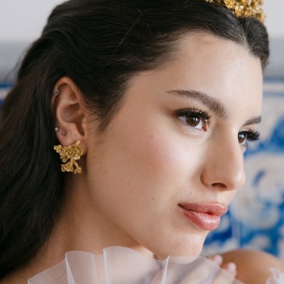 Mulher com tiara e brincos dourados florais e vestido branco com tecido translúcido