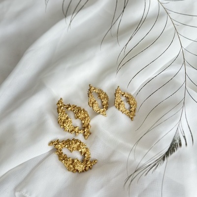 Brincos dourados com textura sobre tecido branco com padrão linear cinza