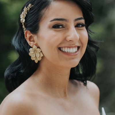 Mulher com presilha dourada, brincos florais dourados e vestido branco texturizado.