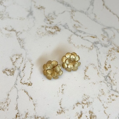 Brincos florais dourados sobre superfície branca com veios dourados e cinza