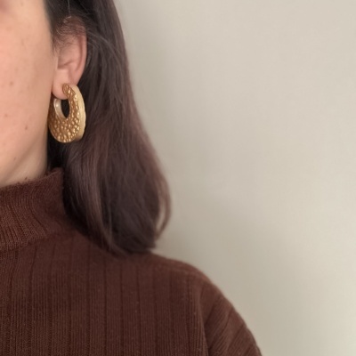 Brincos dourados texturizados usados com suéter castanho