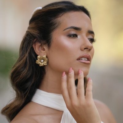 Brincos flor dourados com pérola no centro em mulher com cabelo castanho escuro e vestido branco