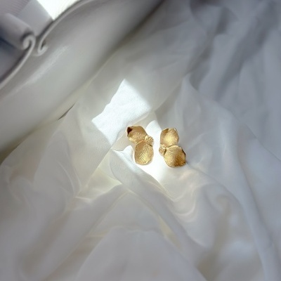 Brincos dourados em formato de pétalas sobre tecido branco
