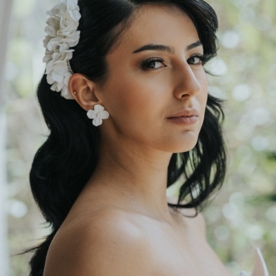 Mulher com presilha e brinco de flores brancas, cabelo preto, fundo claro desfocado