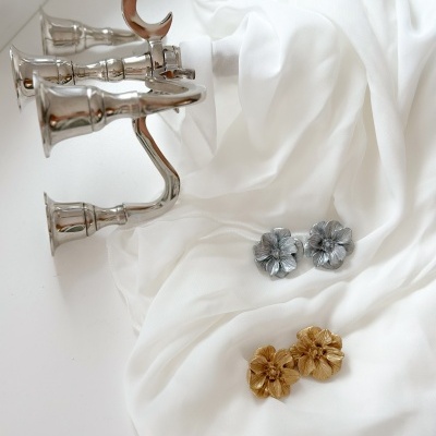 Dois pares de brincos florais dourados e prateados sobre tecido branco com suporte metálico