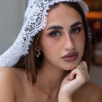 Mulher com lenço de renda branca na cabeça, brincos dourados e anel delicado