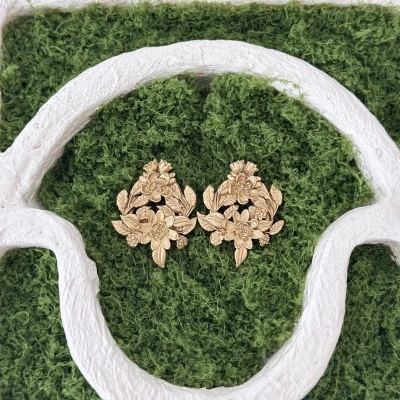 Brincos dourados florais em fundo verde felpudo com moldura branca.