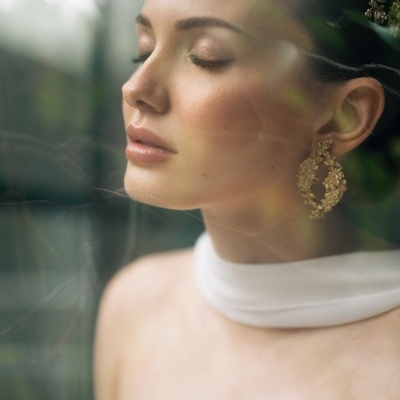 Mulher com tiara dourada e brincos grandes dourados usando top branco com gola alta