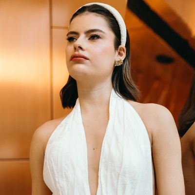 Mulher com vestido branco e banda branca na cabeça, fundo laranja metálico