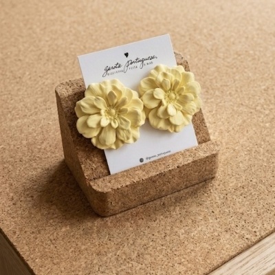 Brincos de flores amarelas em suporte de cortiça sobre mesa.