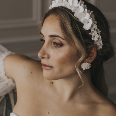 Mulher com tiara branca de flores e brincos florais combinando, vestindo vestido branco