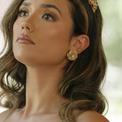 Mulher com coroa e brincos dourados em ambiente claro
