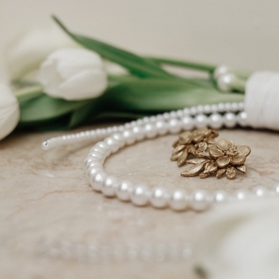 Colar de pérolas com broche dourado e tulipas brancas ao fundo
