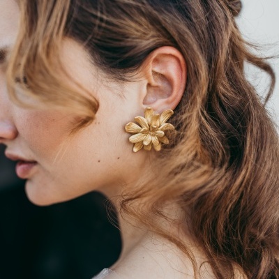 Brincos florais dourados em detalhe no ouvido de mulher com cabelo castanho claro