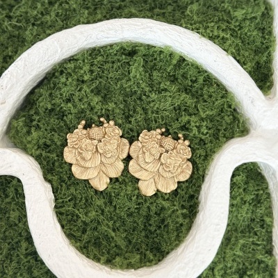 Brincos dourados florais sobre textura verde com estrutura branca