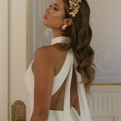 Mulher com vestido branco de costas abertas e acessórios dourados numa sala elegante