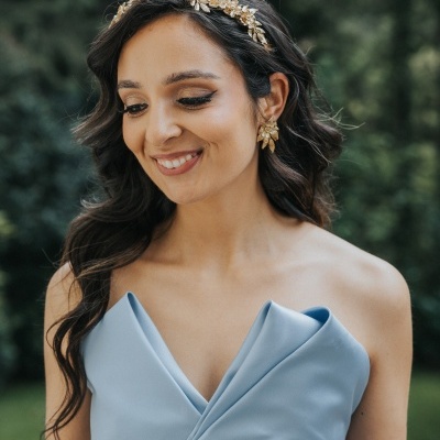 Mulher com vestido azul claro e acessórios dourados em ambiente exterior