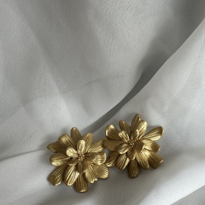 Brincos dourados em forma de flores sobre tecido branco