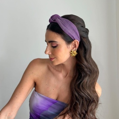 Mulher com faixa de cabelo roxa e brincos dourados grandes