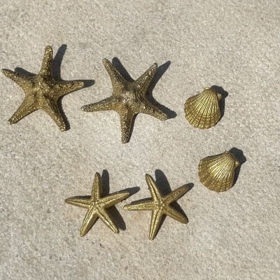 Oito objetos decorativos dourados em forma de estrela-do-mar e concha sobre superfície clara