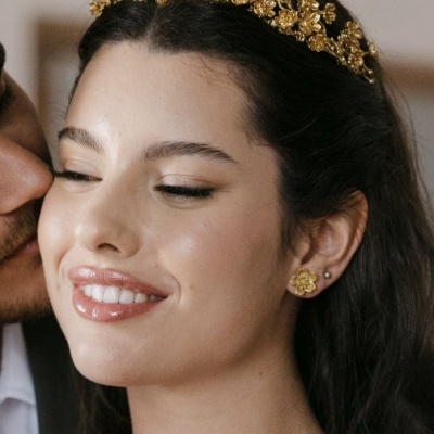 Mulher com tiara dourada floral e brincos dourados em ambiente interno