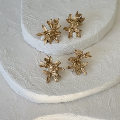 Brincos dourados com design floral e pérolas em bases brancas texturizadas