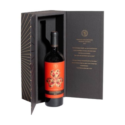Garrafa de vinho tinto em caixa preta aberta com rótulo vermelho e texto dourado