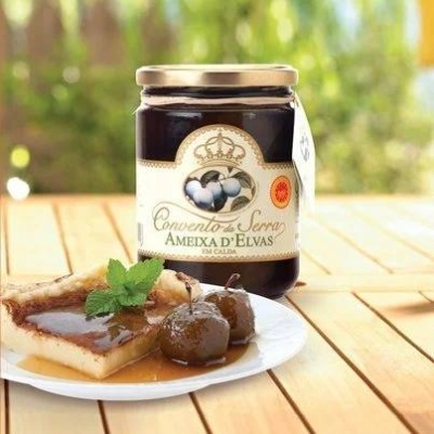 Frasco de amêixa em calda Convento da Serra e prato com pão e ameixas sobre mesa de madeira