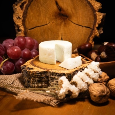 Queijo branco sobre base de madeira rodeado por uvas, castanhas, nozes e planta seca