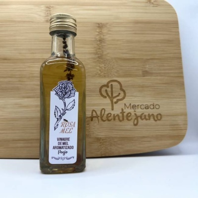 Garrafa de vinagre de mel aromatizado com rótulo branco e tampa dourada em tábua de madeira