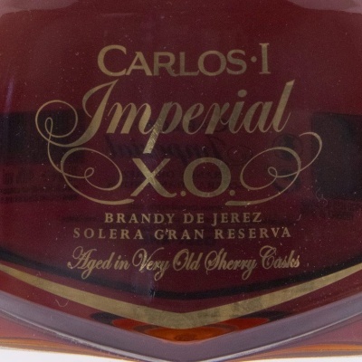 Garrafa de brandy Carlos I Imperial X.O. com rótulo dourado em fundo escuro