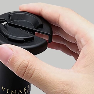 Mão segurando cortador preto num gargalo de garrafa de vinho.