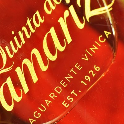 Rótulo dourado em garrafa vermelha com texto Quinta do Jamariz, aguardente, est. 1926