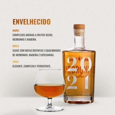 Frasco de bebida alcoólica com rolha e copo com líquido âmbar em fundo claro e texto descritivo em português.