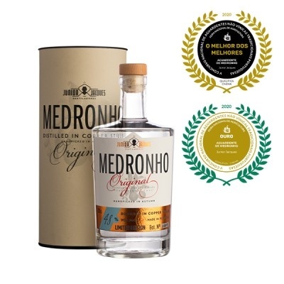 Garrafa de Medronho Original junto à embalagem cilíndrica e dois emblemas de prémios de 2020