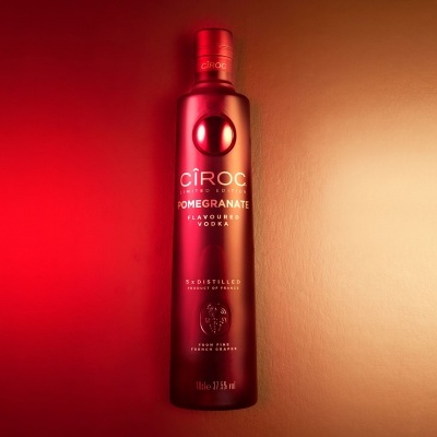 Garrafa vermelha metálica de vodka CÎROC Pomegranate sobre fundo degradê vermelho para bege