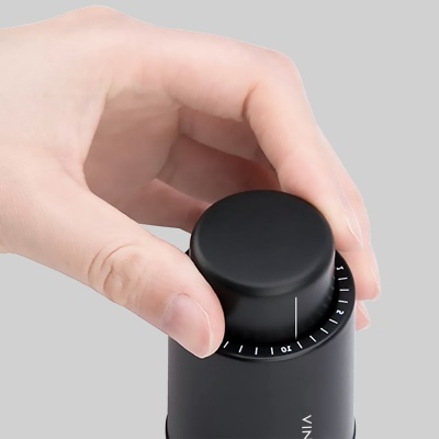 Mão ajustando botão de moinho preto com marcações numéricas sobre fundo cinza