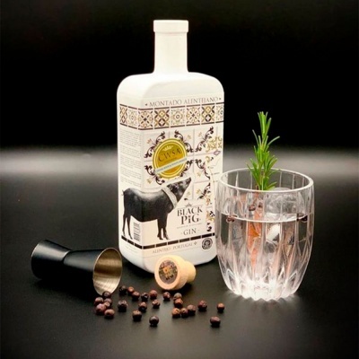 Garrafa de gin Black Pig, copo com bebida e alecrim, pilão e bagas sobre fundo preto