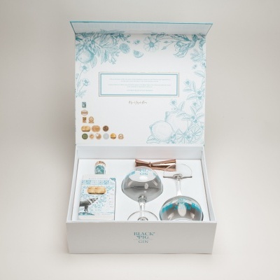 Caixa branca aberta com taças de vidro espelhado, funil de metal cobre e pequena caixa decorativa