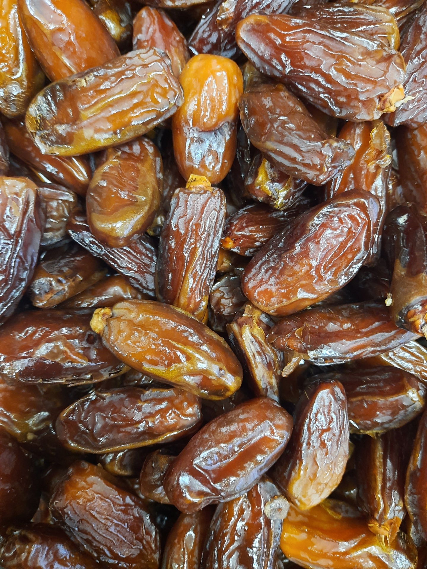 Tâmaras secas castanho-escuro a castanho-claro com textura brilhante e rugosa, empilhadas