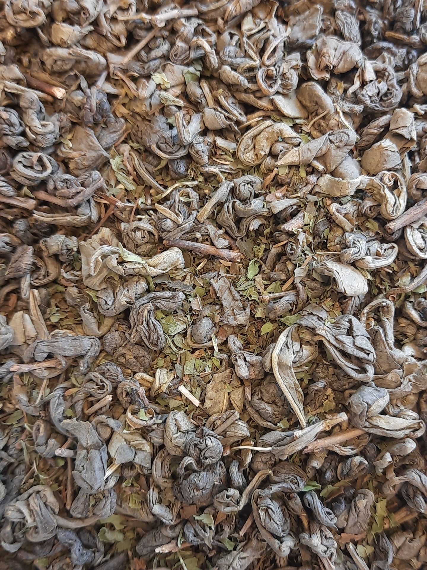 Folhas de chá secas e enroladas castanhas e verdes com textura rugosa