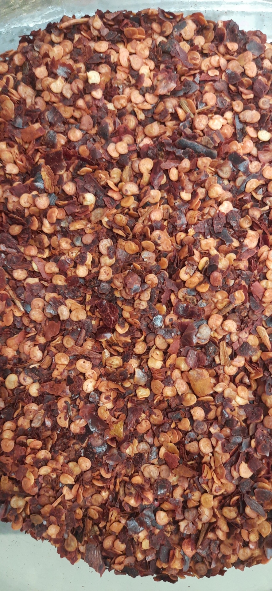 Flocos de pimenta vermelha seca com sementes visíveis numa superfície transparente