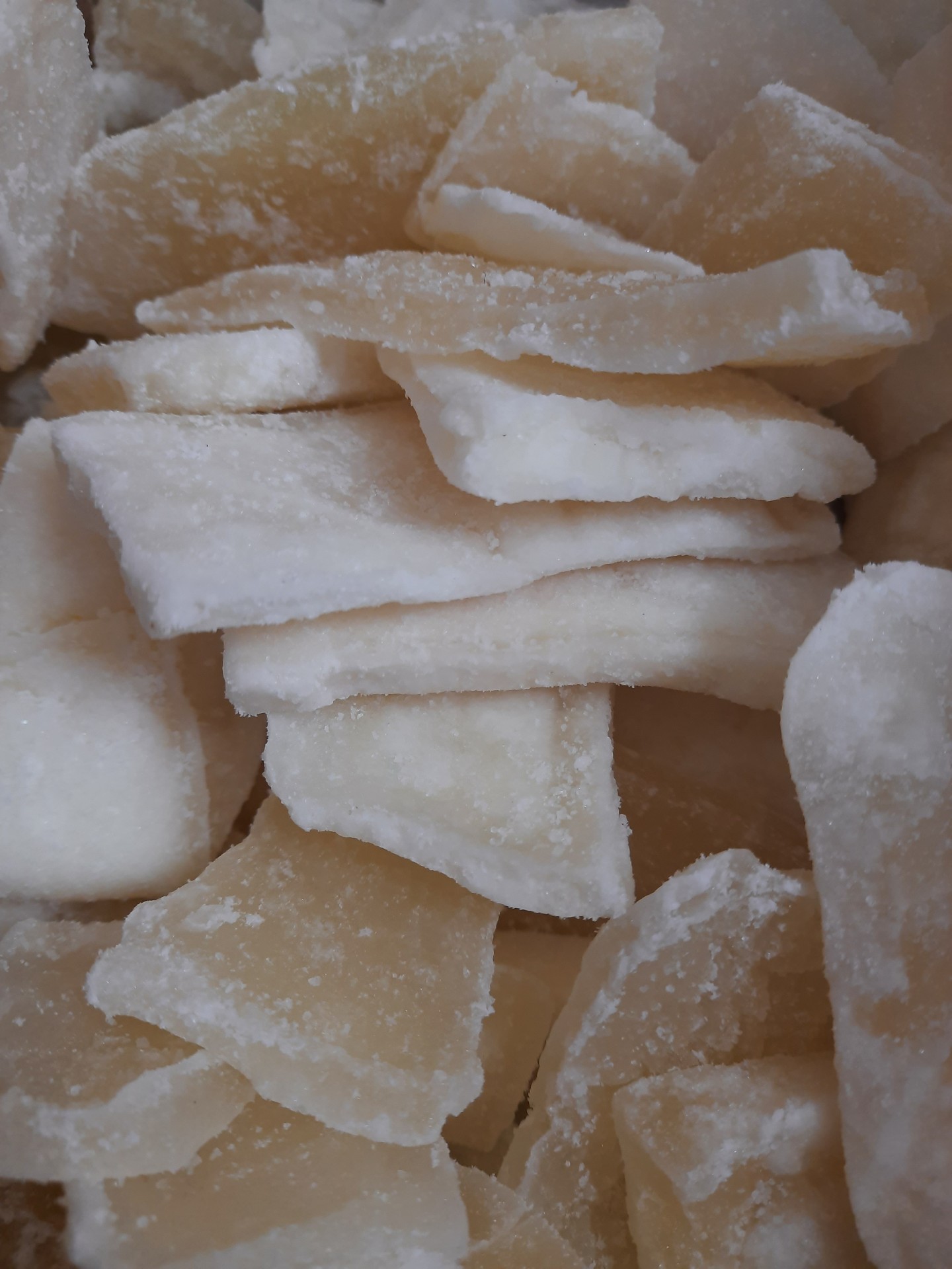 Pedaços irregulares de côco seco e açucarado, cor branca e amarelada