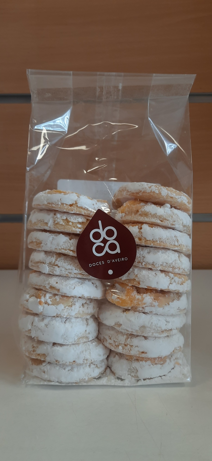 Pacote transparente com bolachas cobertas de açúcar em pó e rótulo 'doca DOCES D'AVEIRO'
