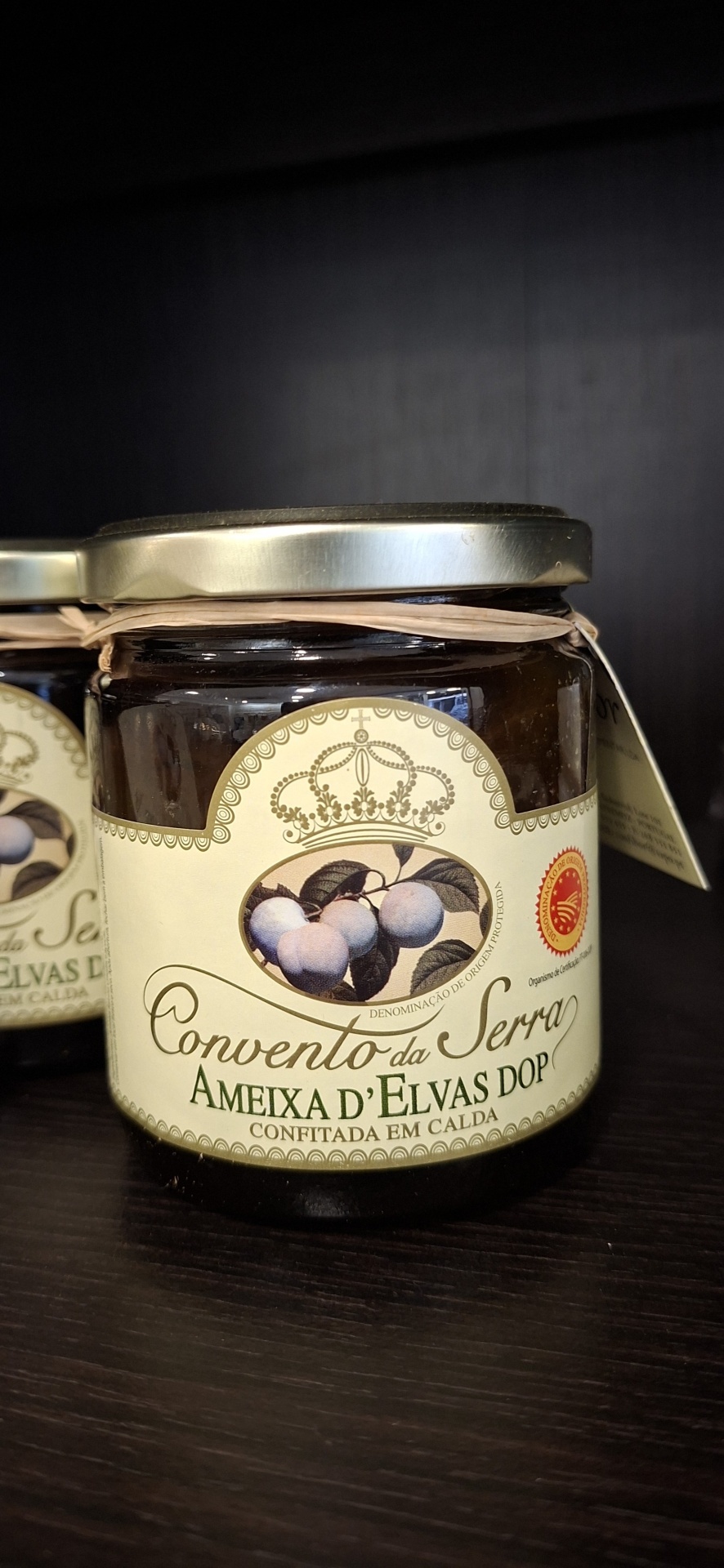 Frasco de vidro com ameixas d'Elvas em calda com rótulo creme e selo de origem